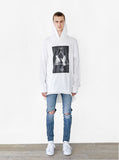 Head to toe shot of Balance Triangle Long-Sleeve Hooded Tee in White paired with ripped blue denim 